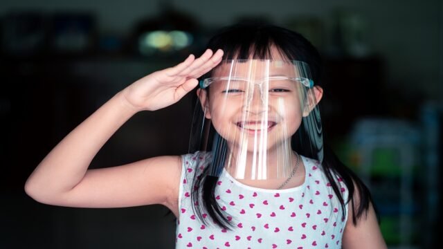 Happy little child girl with a plastic face shield for a virus p