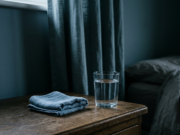 Migraine: The Complete Guide to Causes, Triggers and Relief A folded cool compress and a full glass of water on a bedside table in dim light, illustrating migraine relief