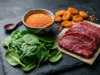 Spinach, red lentils, lean red meat and dried apricots arranged on a dark surface, foods rich in iron