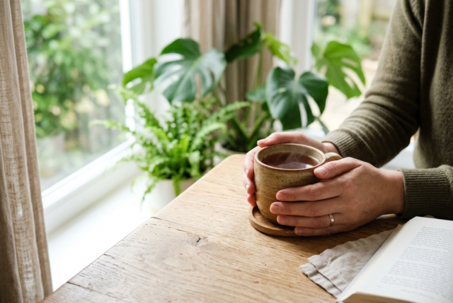 Hands resting around a warm cup of tea beside a window, a calm scene suggesting anxiety relief Hands resting around a warm cup of tea beside a window, a calm scene suggesting anxiety relief