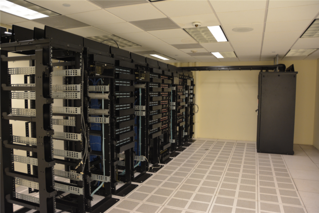 Two rows of server racks with blue indicator lights receding down a data centre corridor Two rows of server racks with blue indicator lights receding down a data centre corridor
