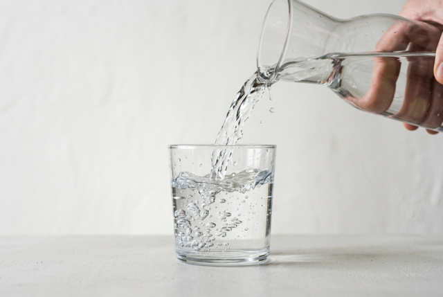 A clear glass of water mid-pour with crisp refraction and rising bubbles