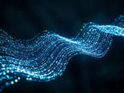 What Is Machine Learning? Types, Examples and Facts Abstract particles glowing blue and white in a flowing wave pattern across a dark background